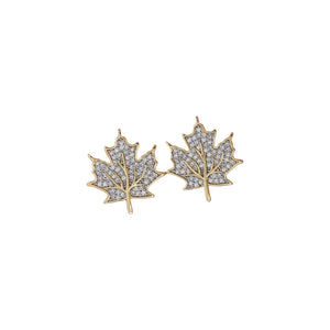 A pair of gold leaf-shaped stud earrings paved with clear stones, held on a person's fingers against a soft pink background.