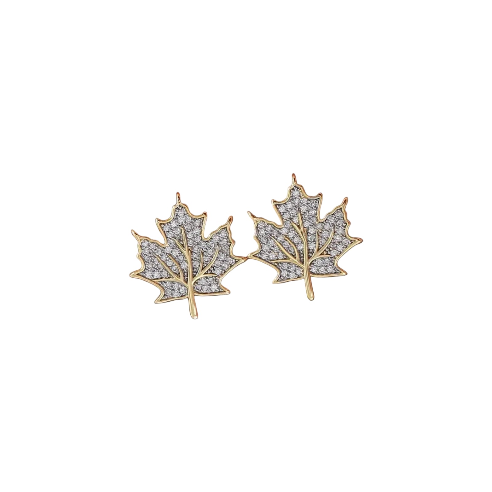 A pair of gold leaf-shaped stud earrings paved with clear stones, held on a person's fingers against a soft pink background.