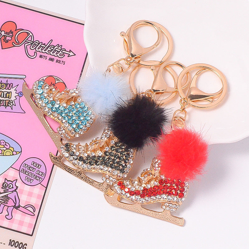 Pink crystal ice skate pom pom keychain on white saucer with blue flowers