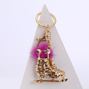 Gold crystal ice skate pom pom keychain on white pyramid – side angle