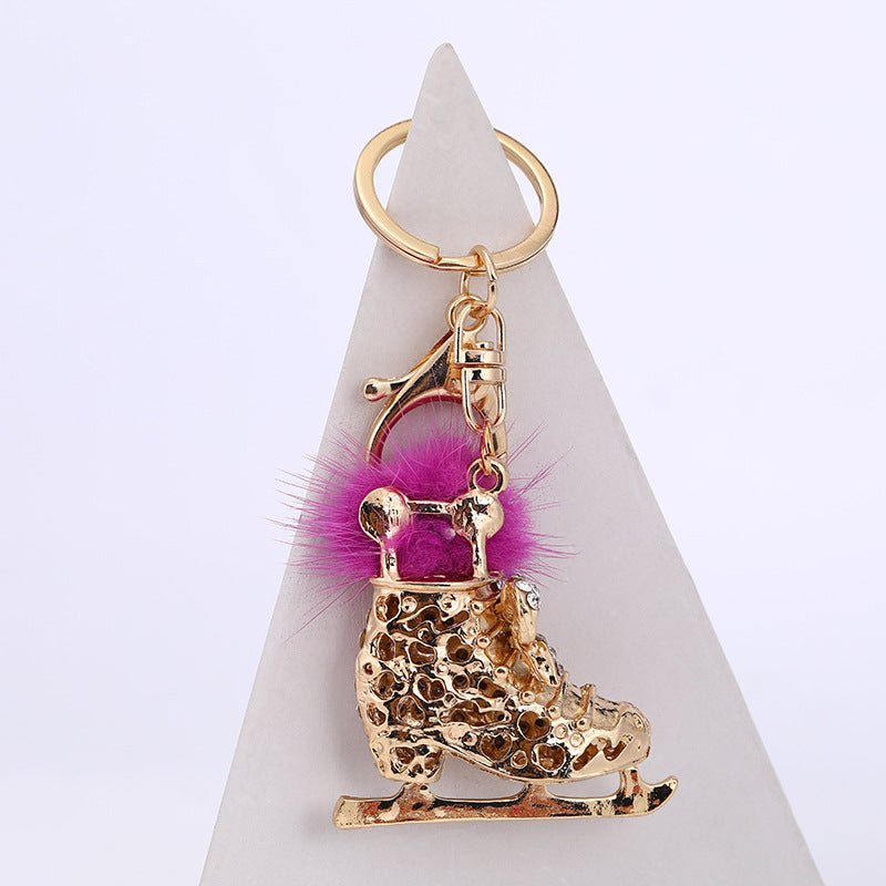 Gold crystal ice skate pom pom keychain on white pyramid – side angle