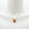 A gold chain necklace with a small bow-shaped pendant featuring red and pink rhinestones, displayed on a white mannequin bust.