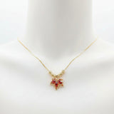 A gold chain necklace with a small bow-shaped pendant featuring red and pink rhinestones, displayed on a white mannequin bust.